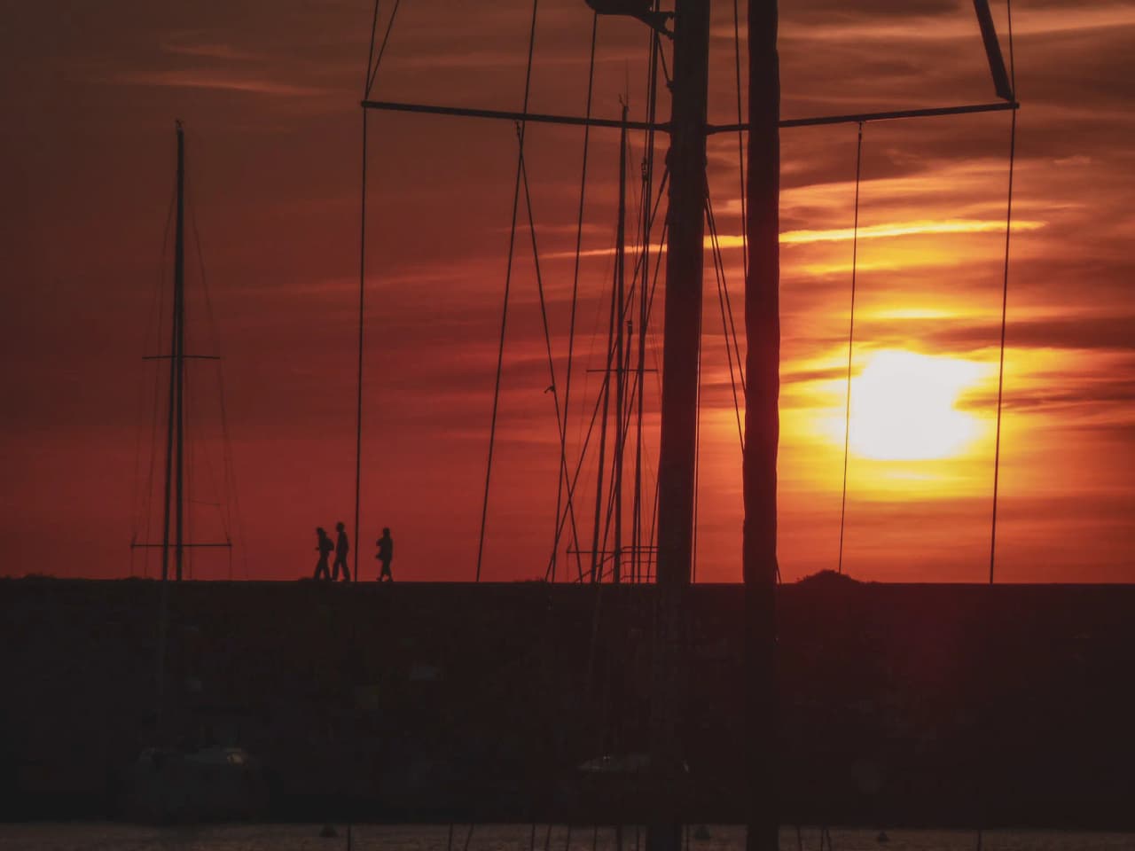 Silhouettes de marcheurs au coucher du soleil, voiliers en arrière-plan, ambiance méditerranéenne.