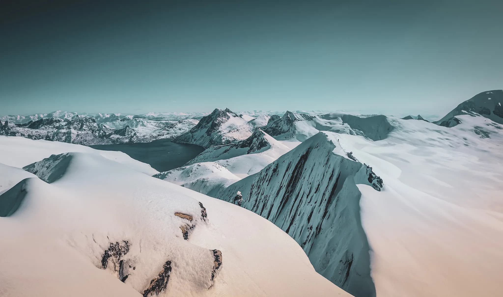 Een majestueus besneeuwd berglandschap, met scherpe pieken en glooiende hellingen. Op de achtergrond zie je een uitgestrekt panorama van bergketens, gedomineerd door steile pieken en