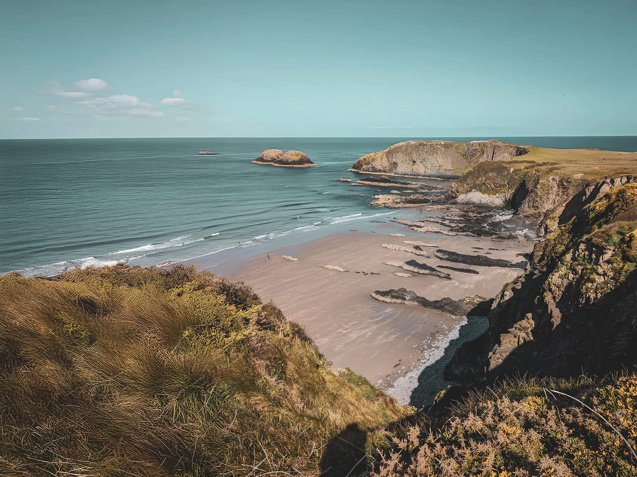 Un panorama côtier spectaculaire des îles galloises, avec des plages de sable et des falaises verdoyantes.