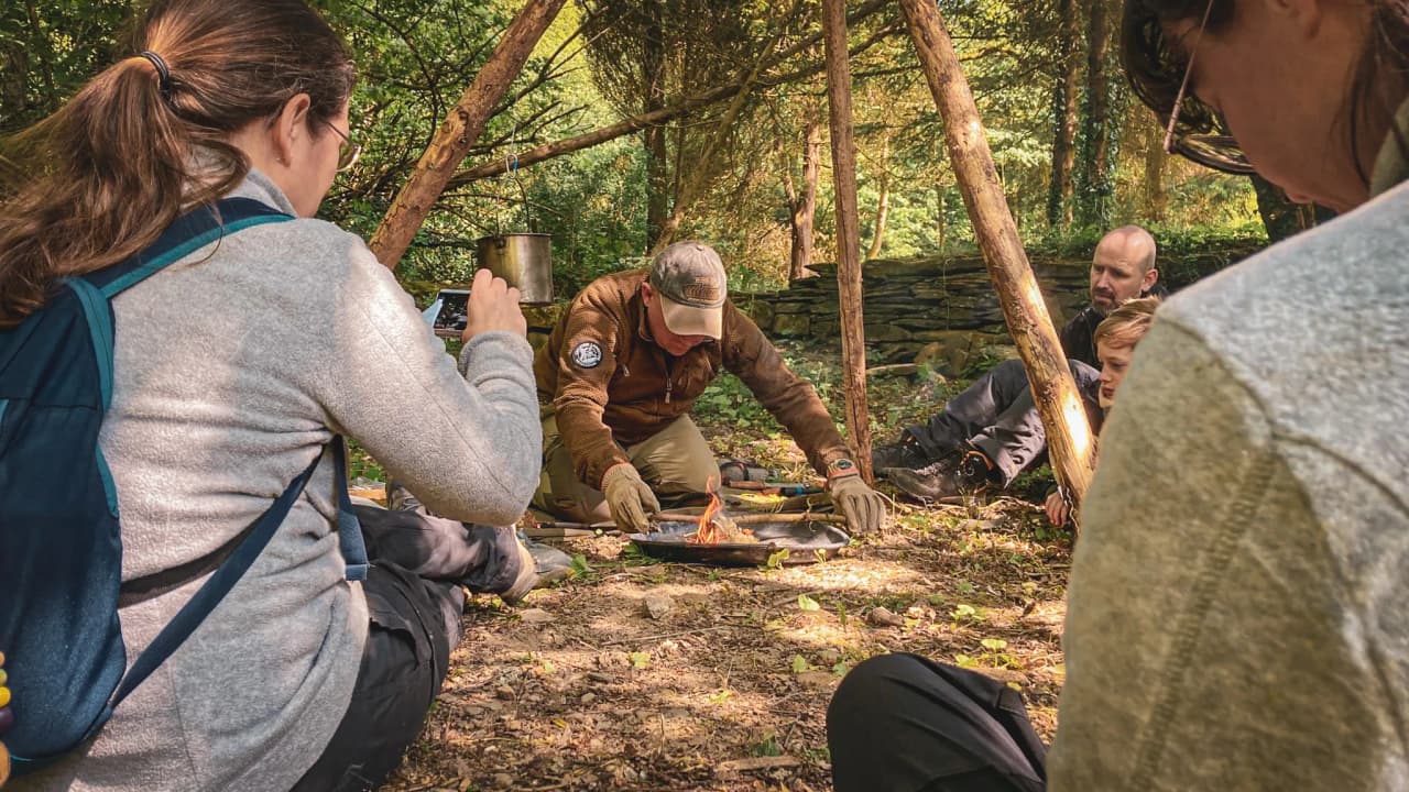 Groupe en pleine nature apprend à allumer un feu, entouré de verdure en Ardenne belge.