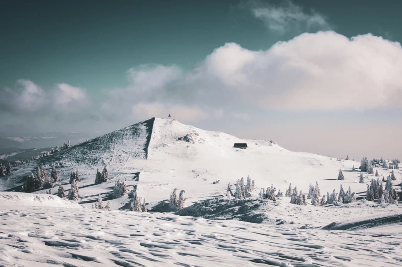 Peyrade enneigé surplombant des forêts, ciel azur et nuages, invitation à l'aventure.