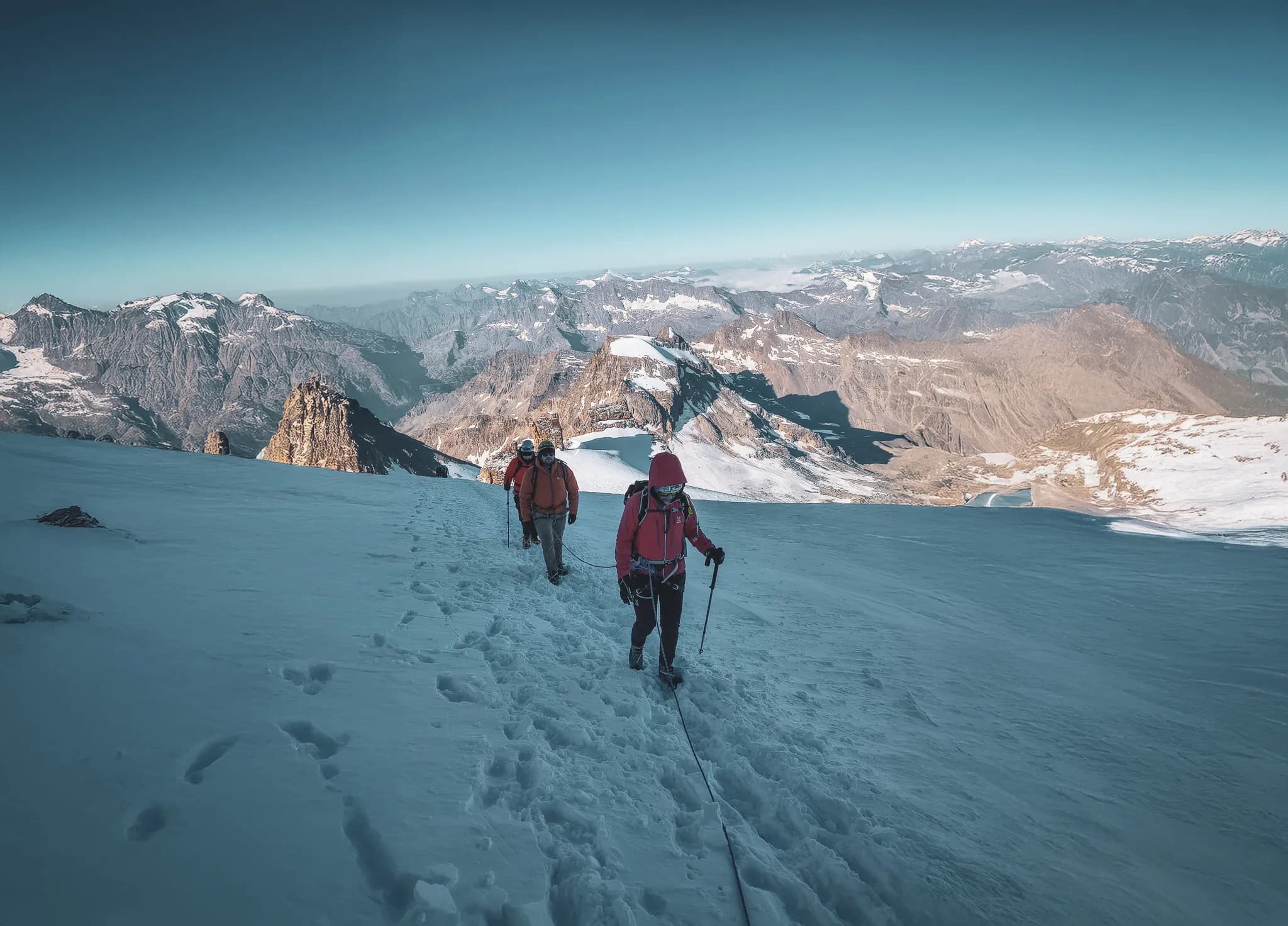 A group climbs a glacier, with majestic peaks in the background. Alpine adventure!
