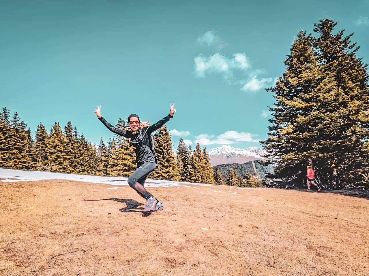 Une coureuse joyeuse dans le Mercantour, entourée de sapins et de montagnes majestueuses.
