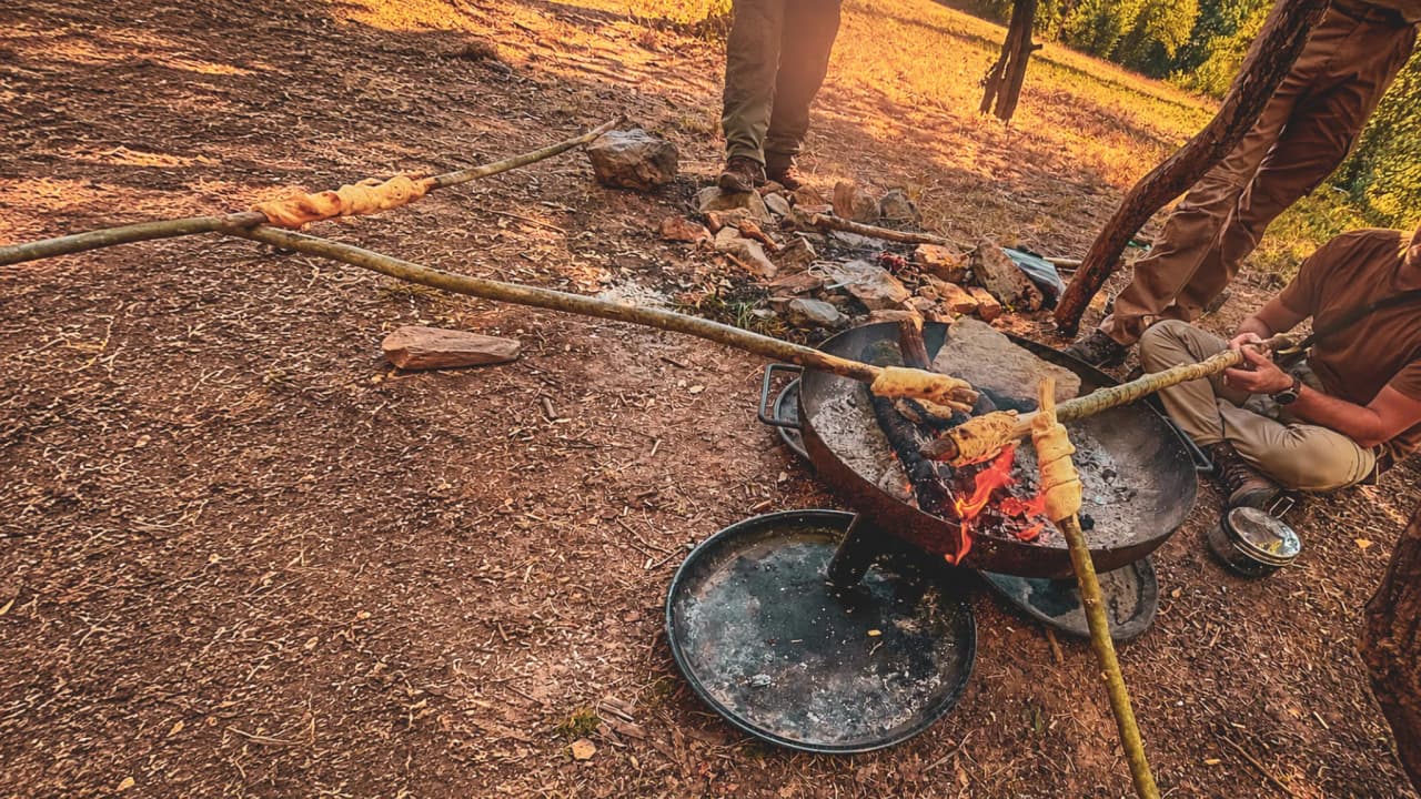 Personnes cuisinant au-dessus d'un feu de camp en pleine forêt, ambiance conviviale et nature.