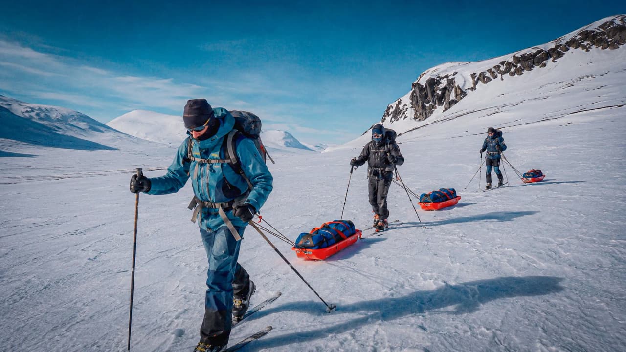 Een groep avonturiers op langlaufski’s die pulka’s voorttrekken door een uitgestrekt besneeuwd landschap in Lapland.