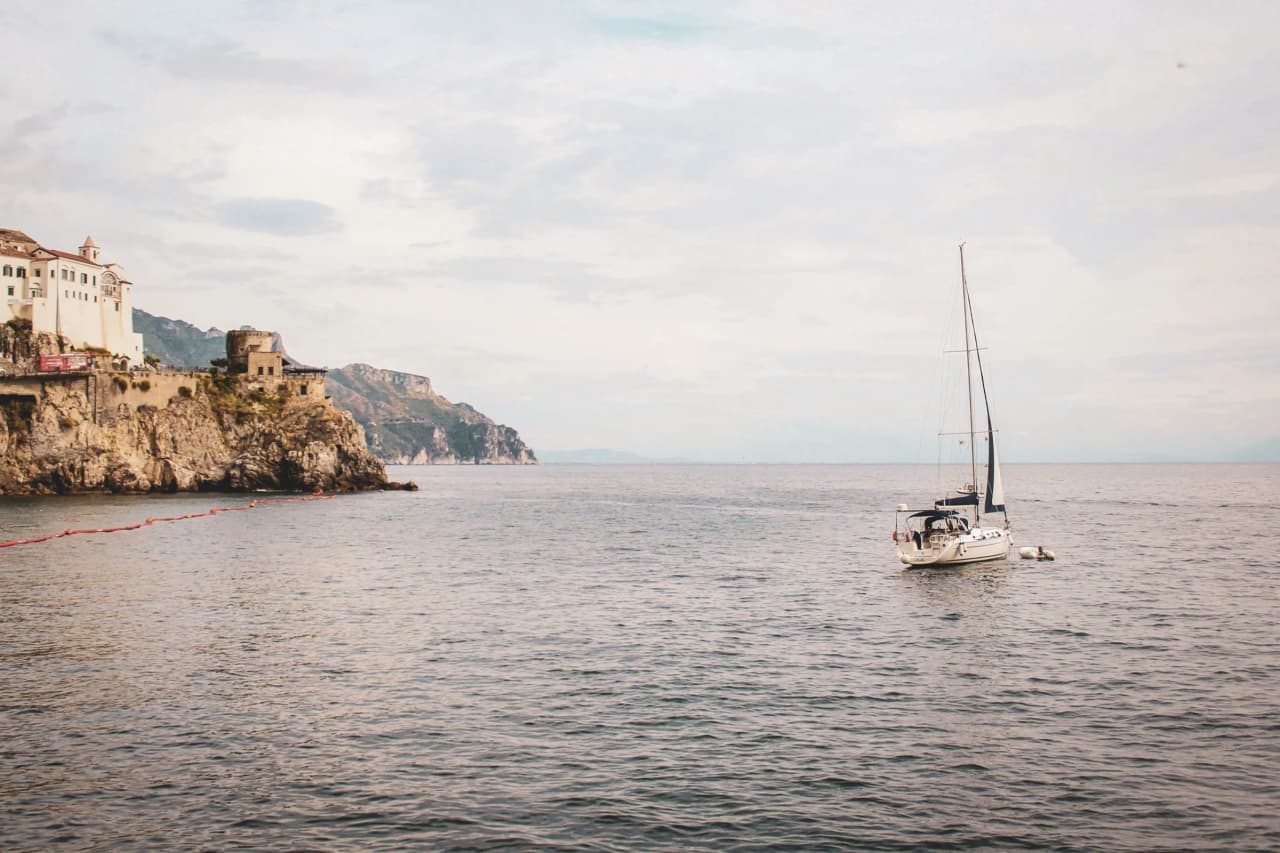 Voilier paisiblement ancré dans une eau turquoise, avec des falaises corses en arrière-plan.