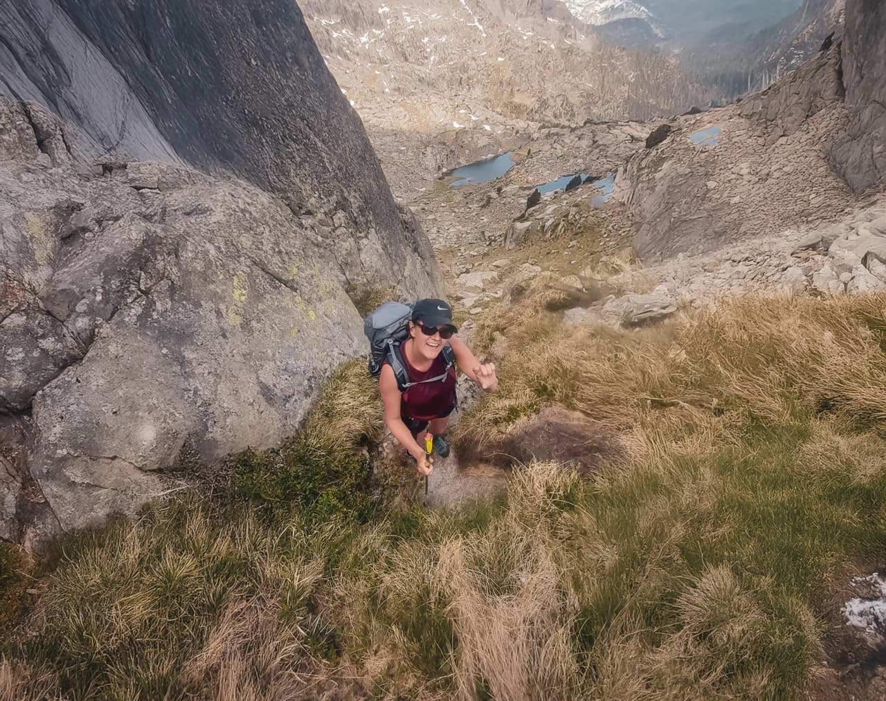 A smiling explorer climbing a rocky path, surrounded by magnificent lakes and mountains.