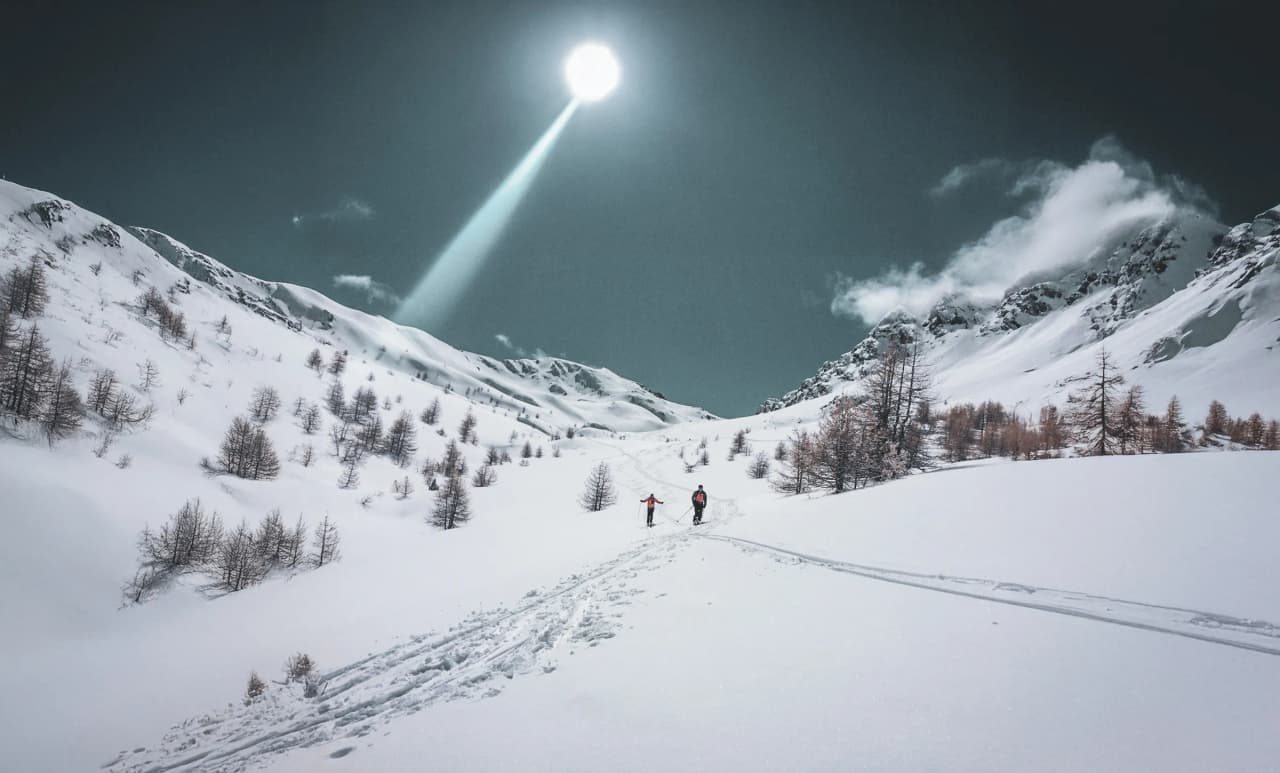 Deux skieurs explorent un paysage alpin enchanteur, sous un ciel lumineux et enneigé.