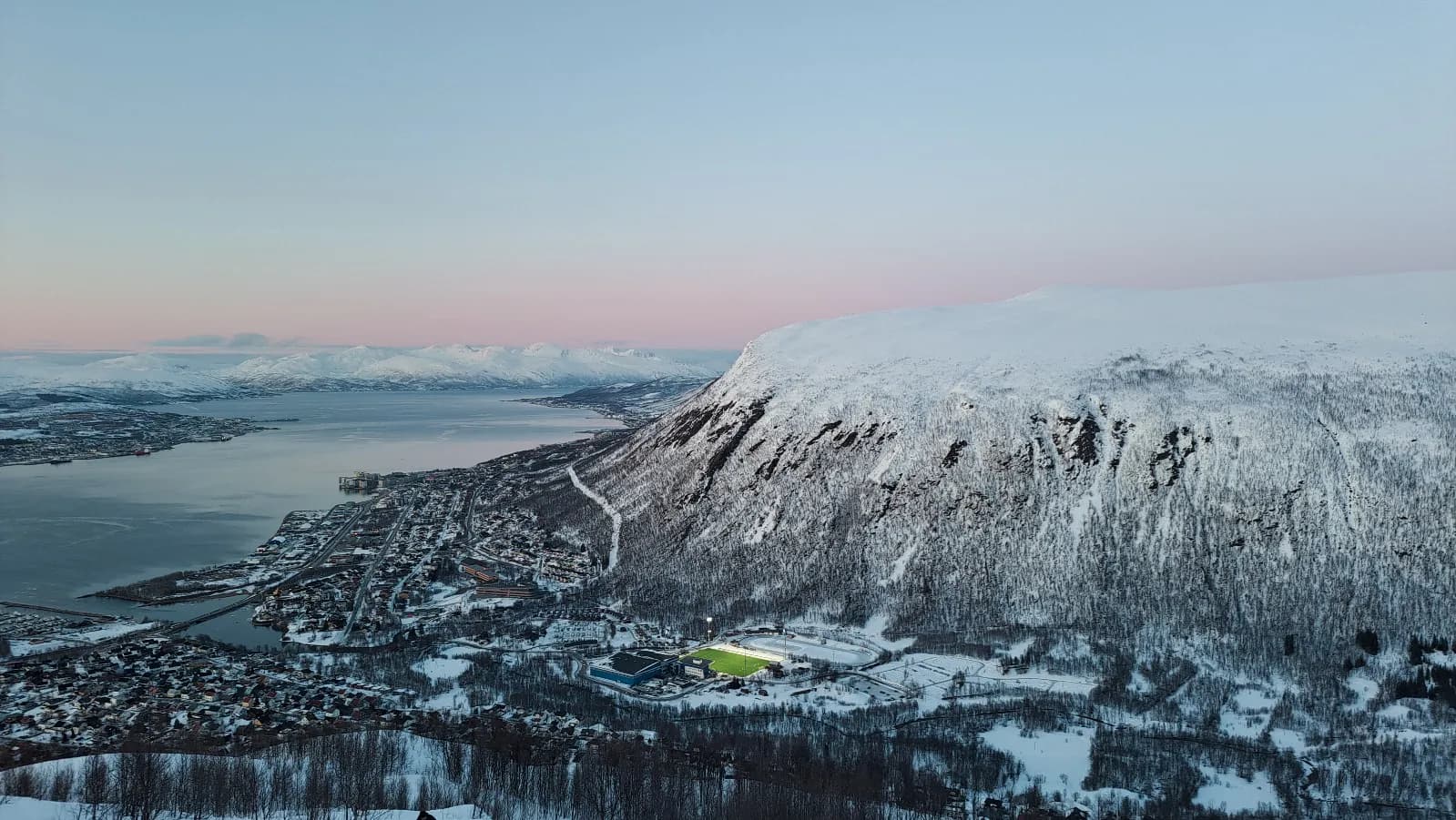 Vue panoramique des fjords de Senja, Norvège, avec paysages enneigés et ciel pastel.