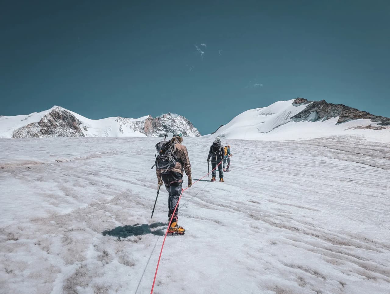 Mountaineers on a glacier, heading towards the majestic Bishorn, under a blue sky.