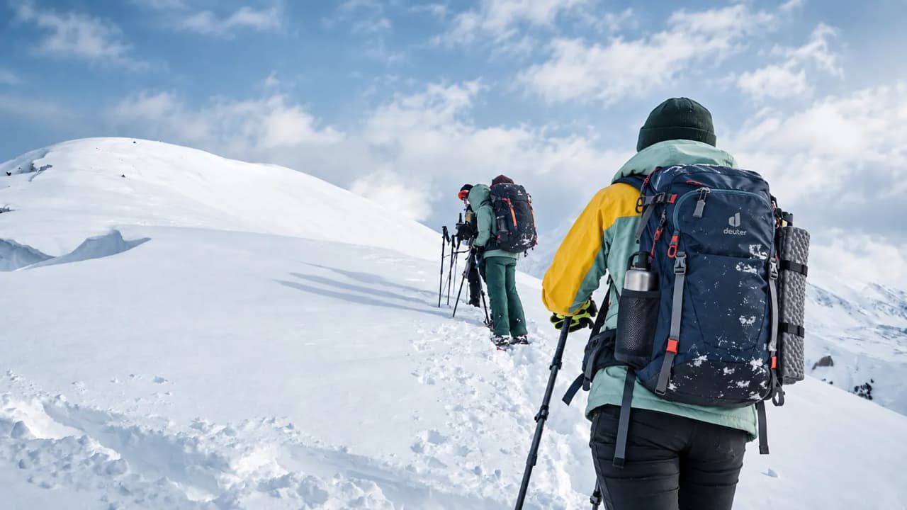 Een groep sneeuwschoenwandelaars die onder een stralende hemel een besneeuwde bergtop beklimt.