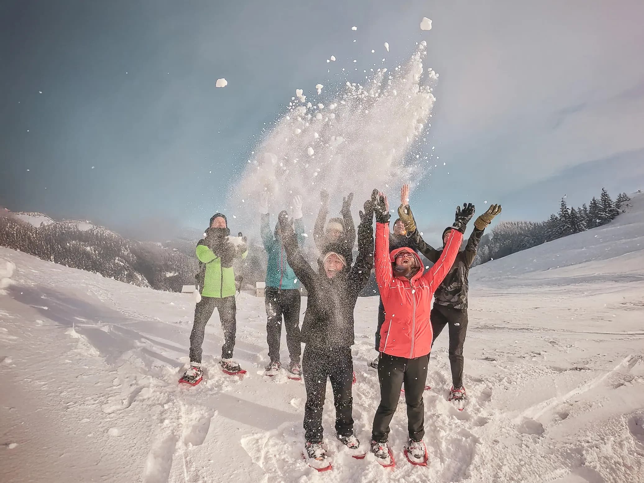 Een enthousiaste groep op sneeuwschoenen, sneeuw aan het gooien onder een zonnige hemel in de Vogezen.