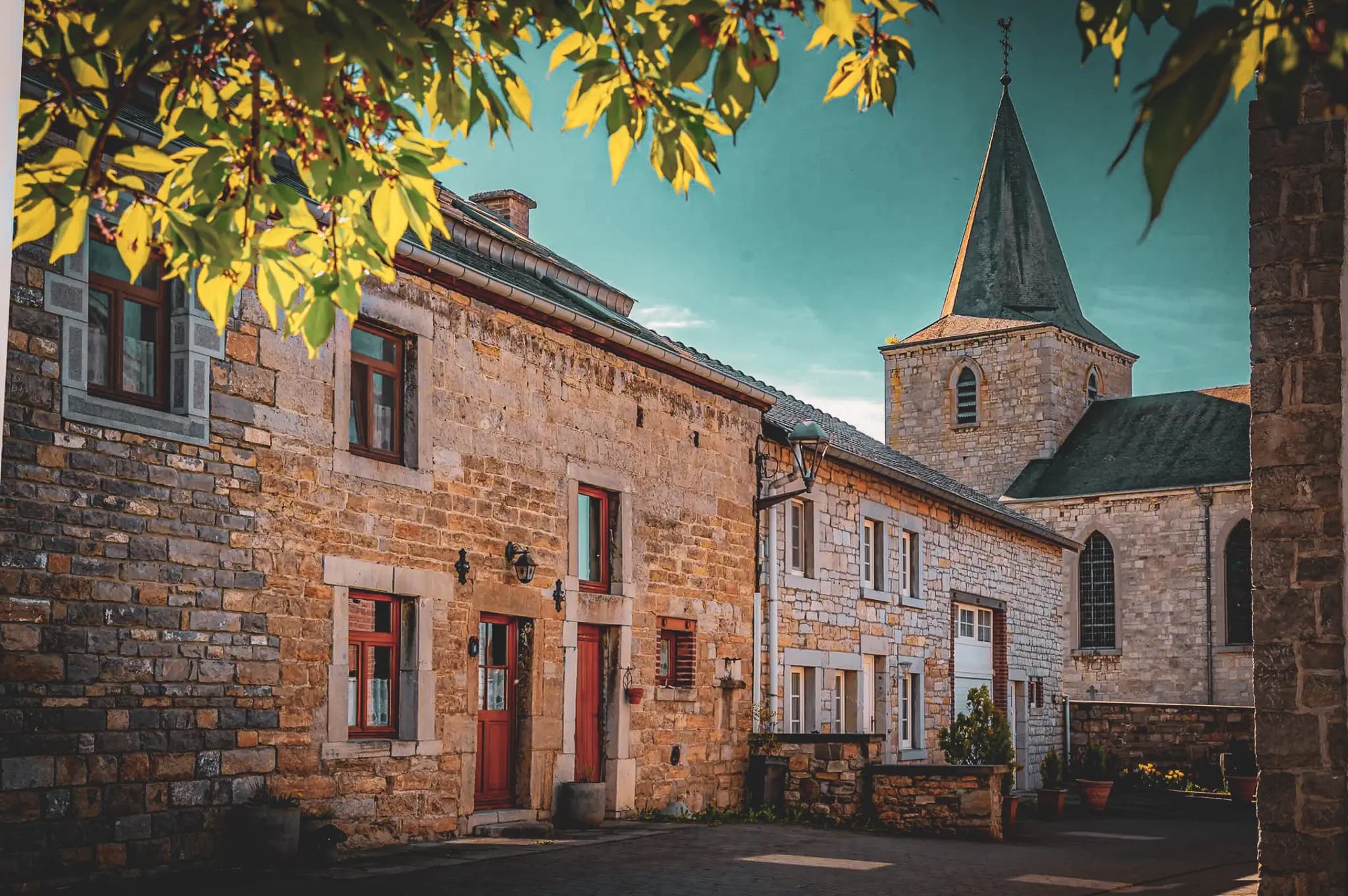 A picturesque village with traditional stone buildings, wood-framed windows and a red door. A slender bell tower can be seen in the background, adding an architectural touch. The scene is illuminated