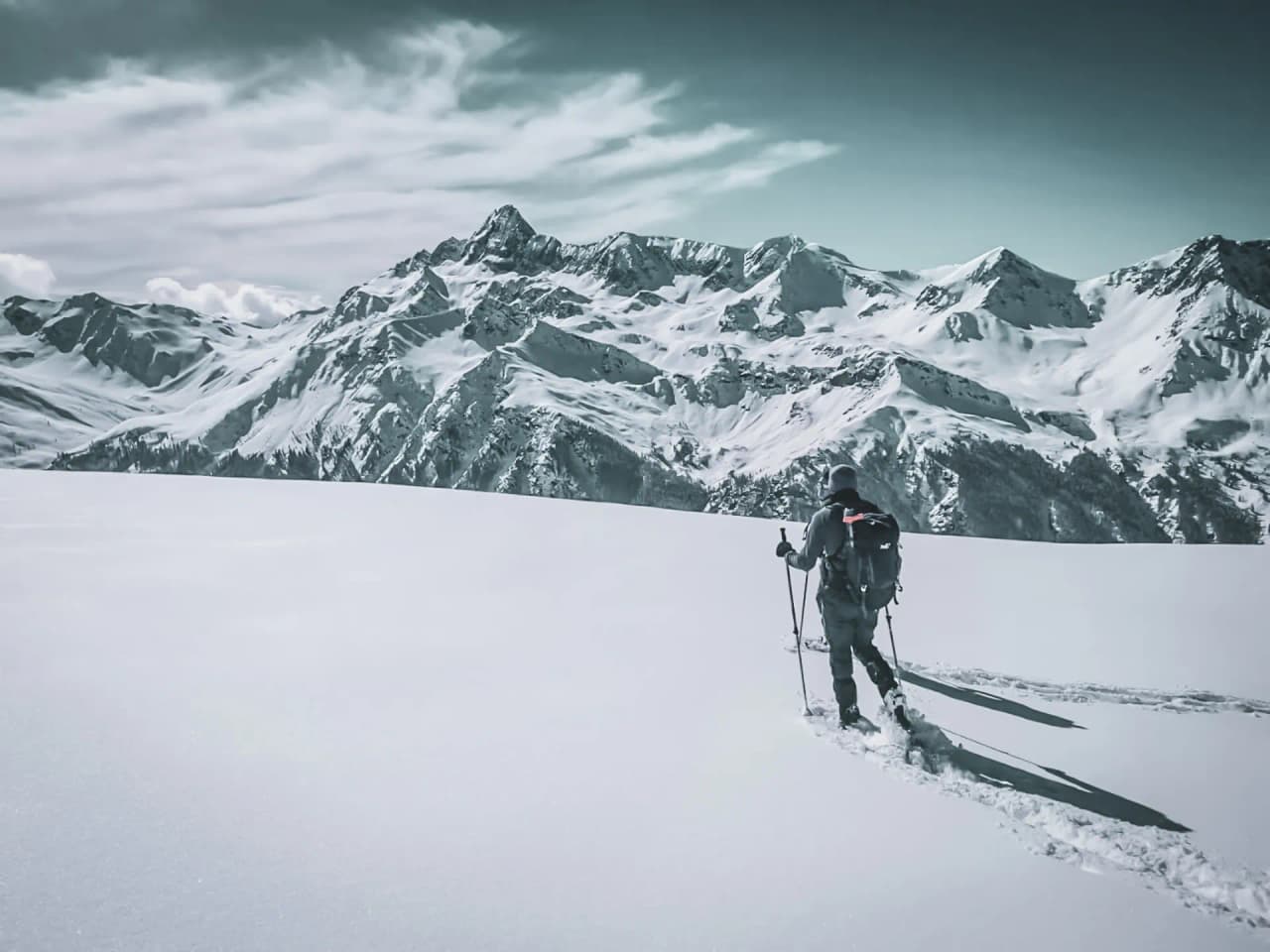 A hiker on snowshoes makes his way through a snow-covered mountain landscape, inviting you to get away from it all.