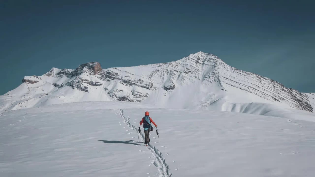 Un skieur s’aventure dans un paysage alpin enneigé, sous un ciel bleu éclatant.