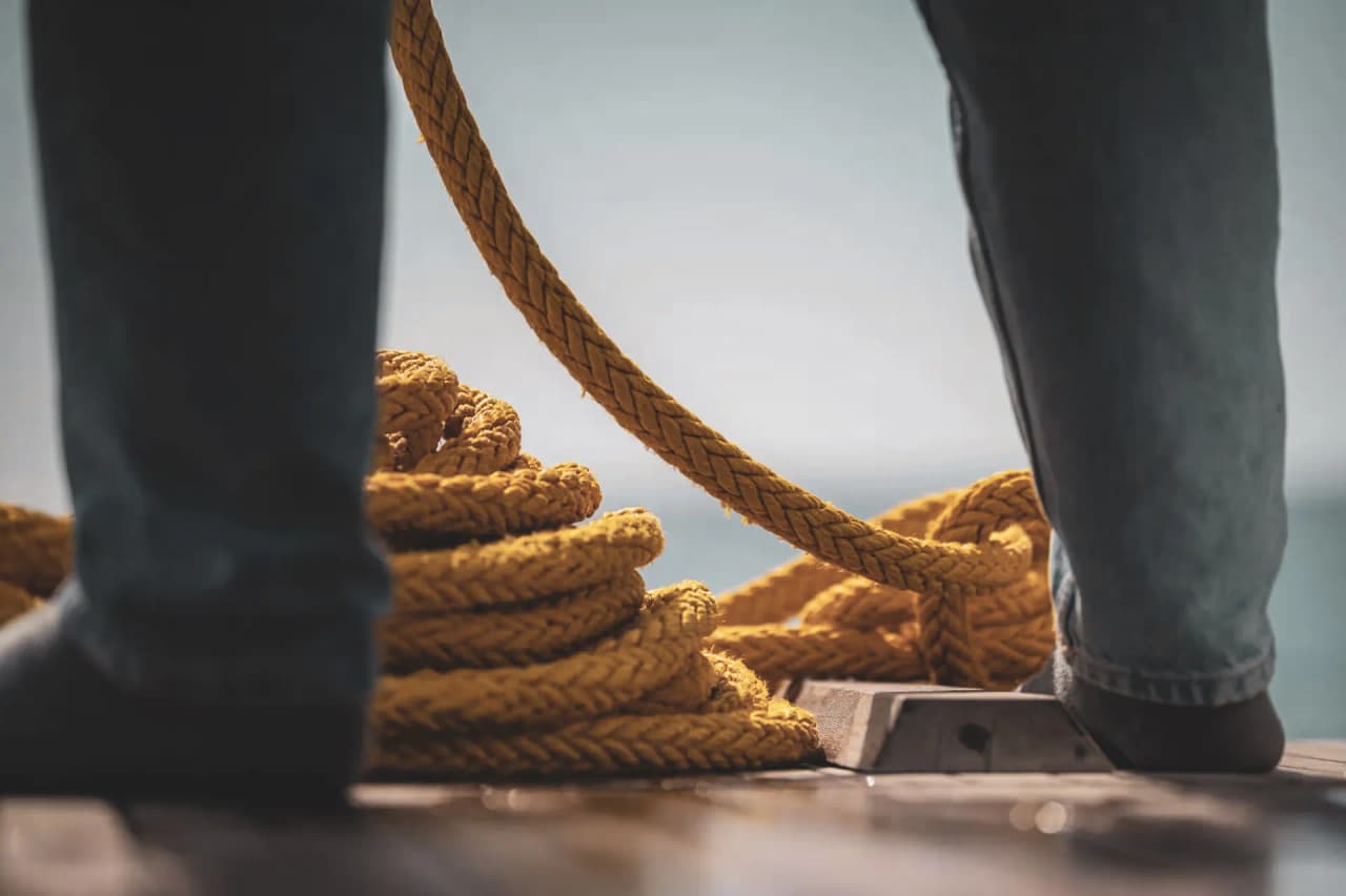 Deux pieds posés sur le pont d'un bateau, près d'une corde jaune, évoquant l'aventure en mer.