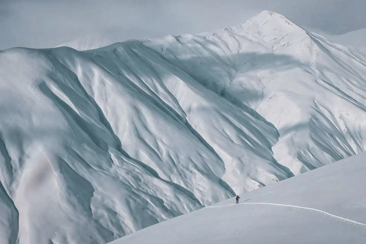 Un skieur solitaire parcourt des pentes enneigées à La Grave, sous un ciel majestueux.