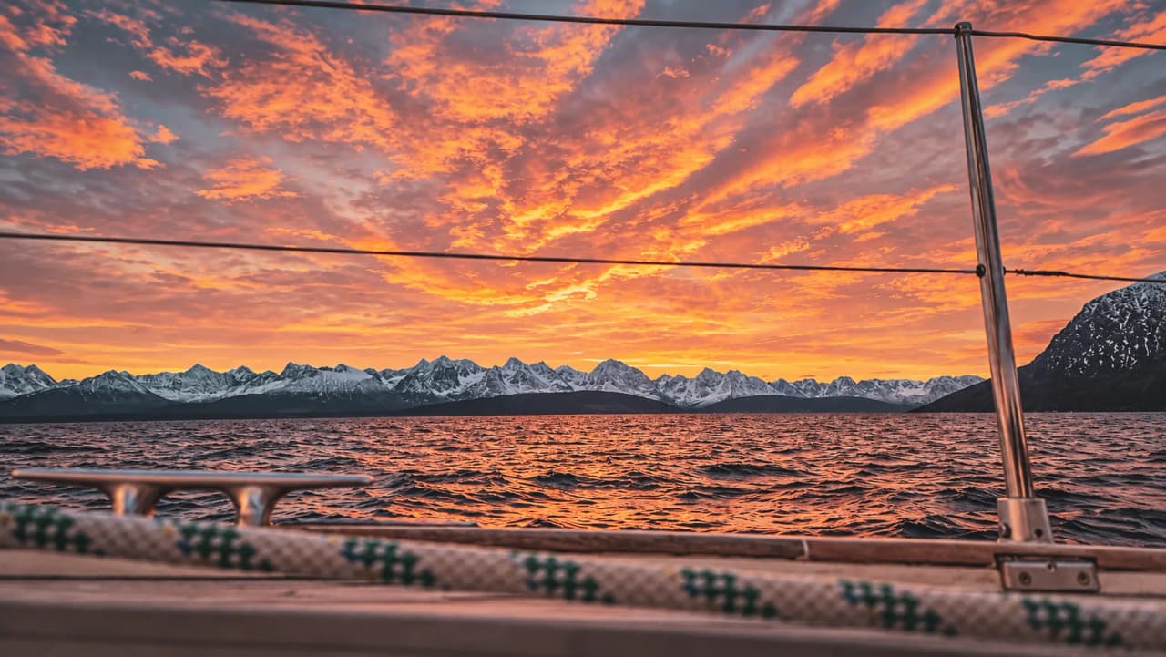 A blazing sunset over snow-capped mountains, a view of the fjords from a sailing boat.
