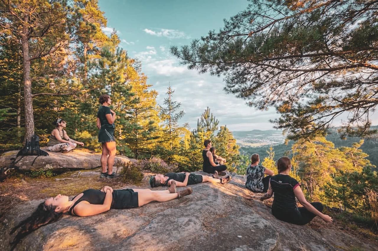 Een groep mensen mediteert op rotsen, omringd door weelderig groen bij zonsondergang.