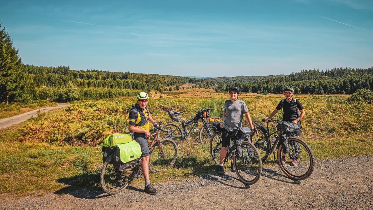 A group of cyclists on a forest track, in front of a green Ardennes landscape.