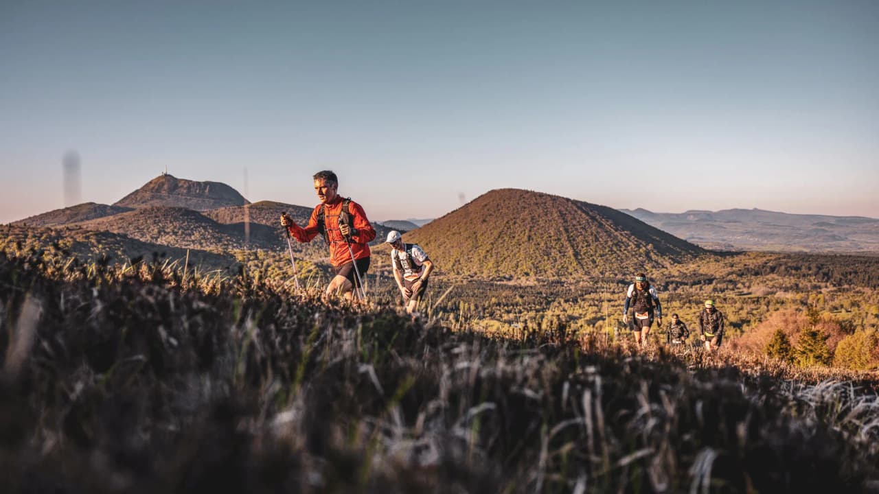 Athletes climbing the volcanoes of the Auvergne, with the lush green landscape as a backdrop.