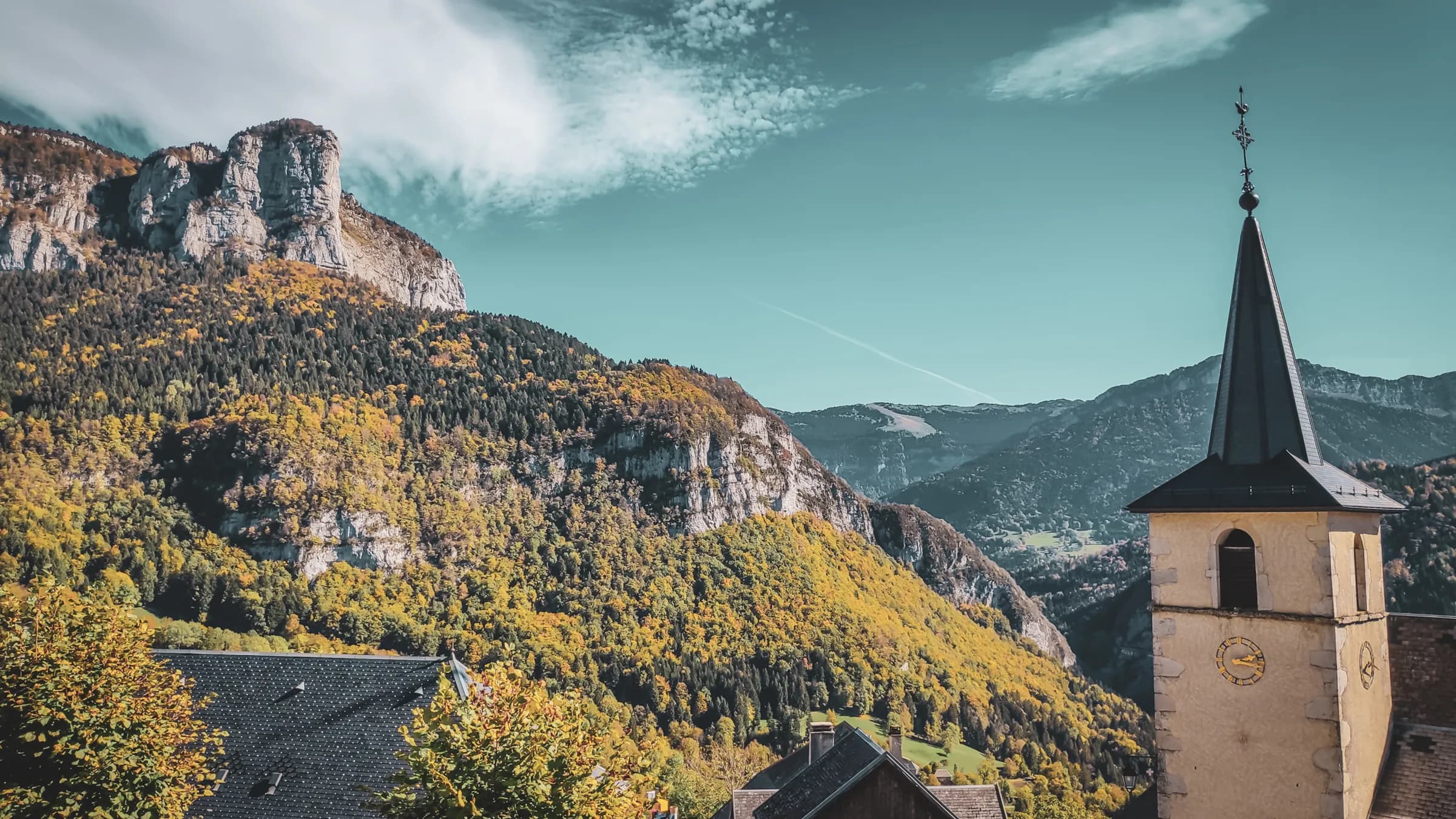 Vue majestueuse des montagnes colorées d'automne, avec un clocher pittoresque au premier plan.