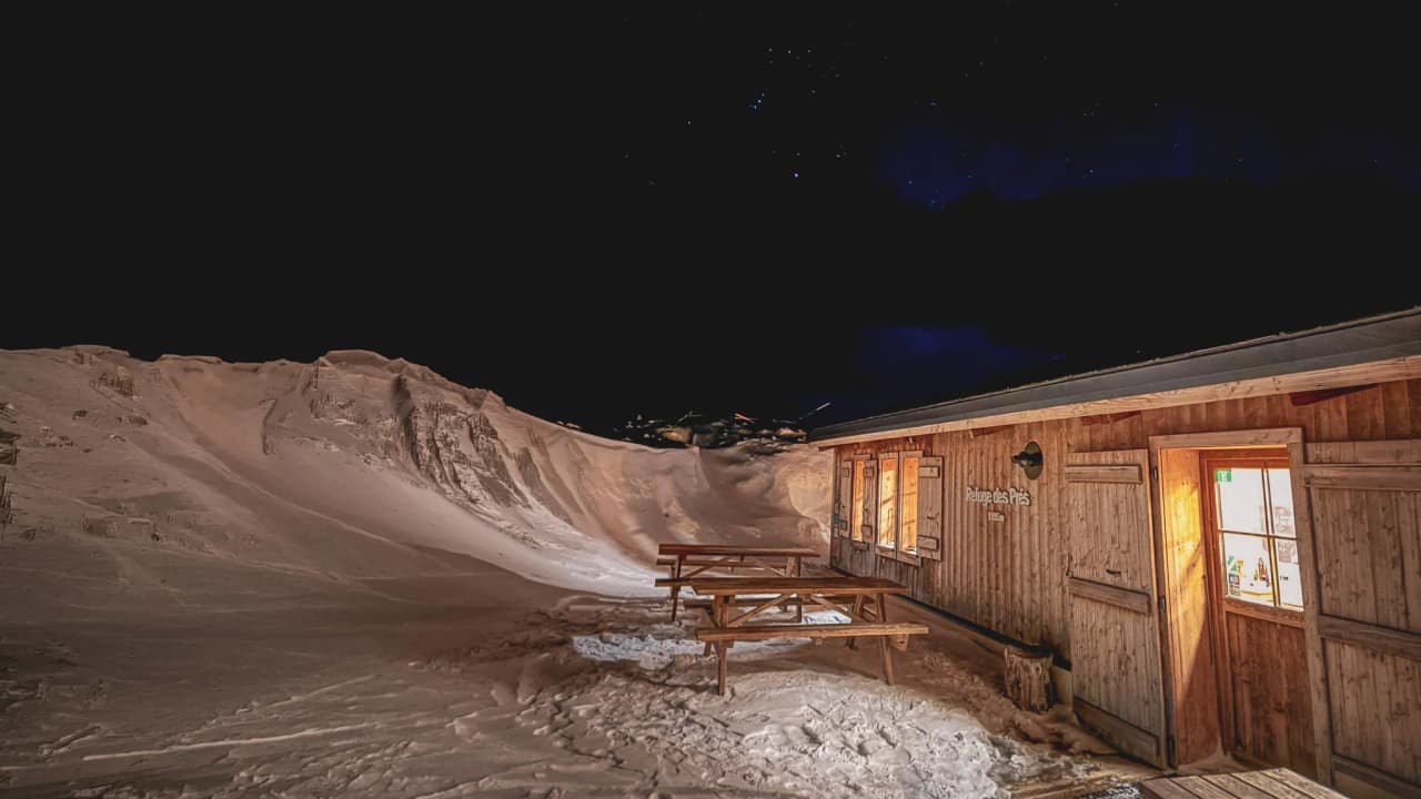 An illuminated wooden Mountain hut, surrounded by snow, under a starry sky. Escape to Mont Blanc.