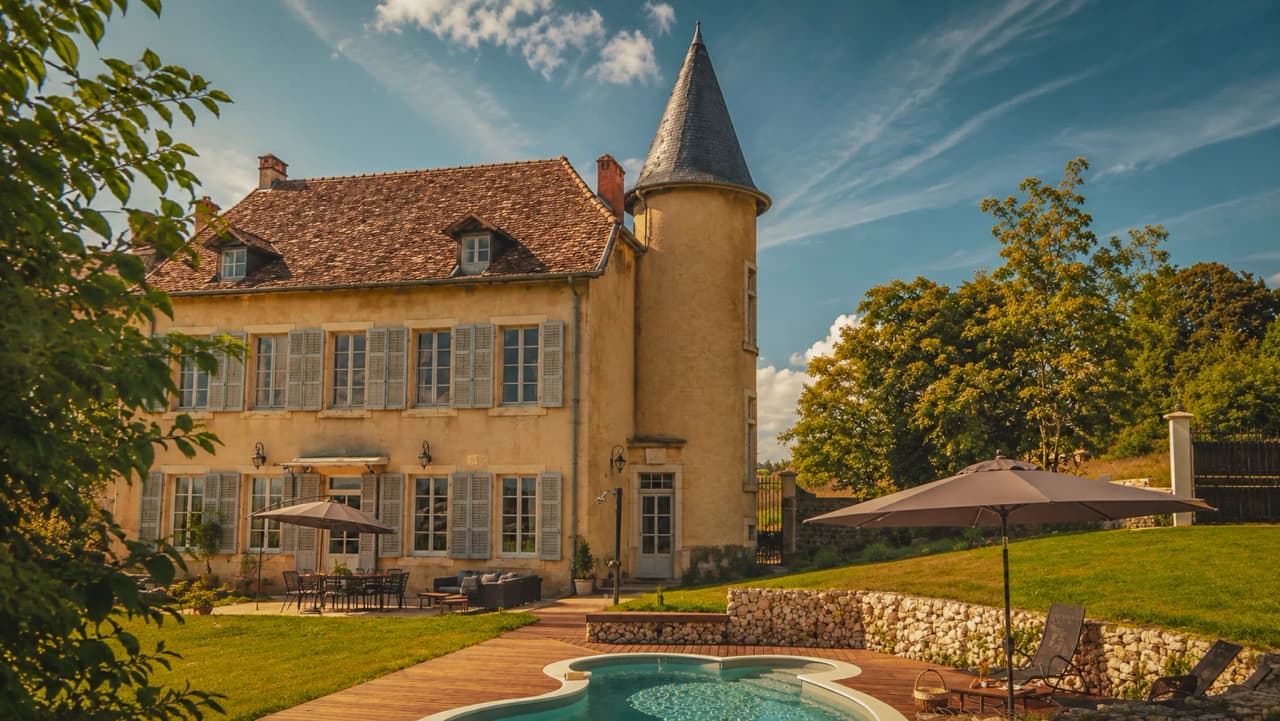 Charming stone house with swimming pool, surrounded by greenery and blue skies, ideal for a relaxing break.