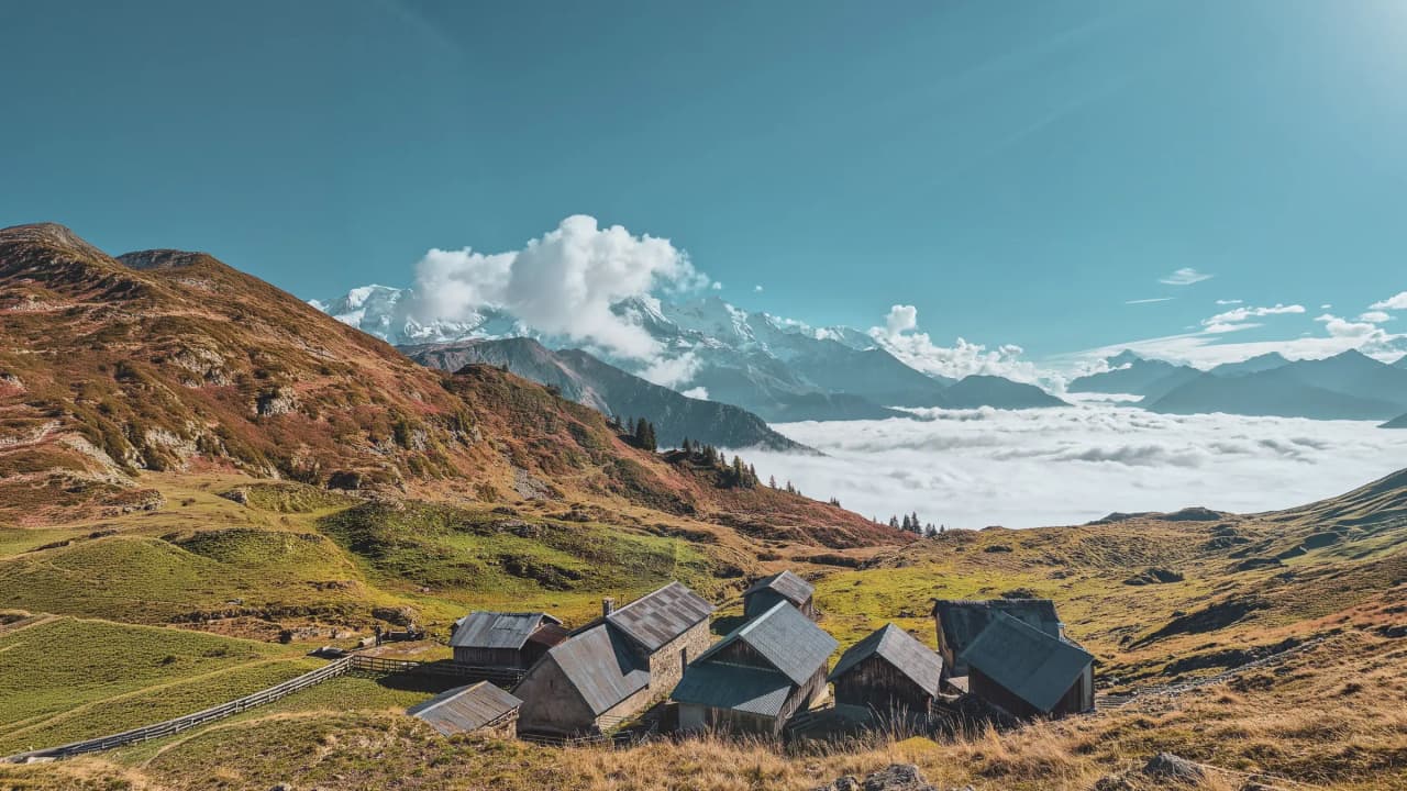 Houten chalets kijken uit over weelderig groene valleien, met uitzicht op besneeuwde bergtoppen.