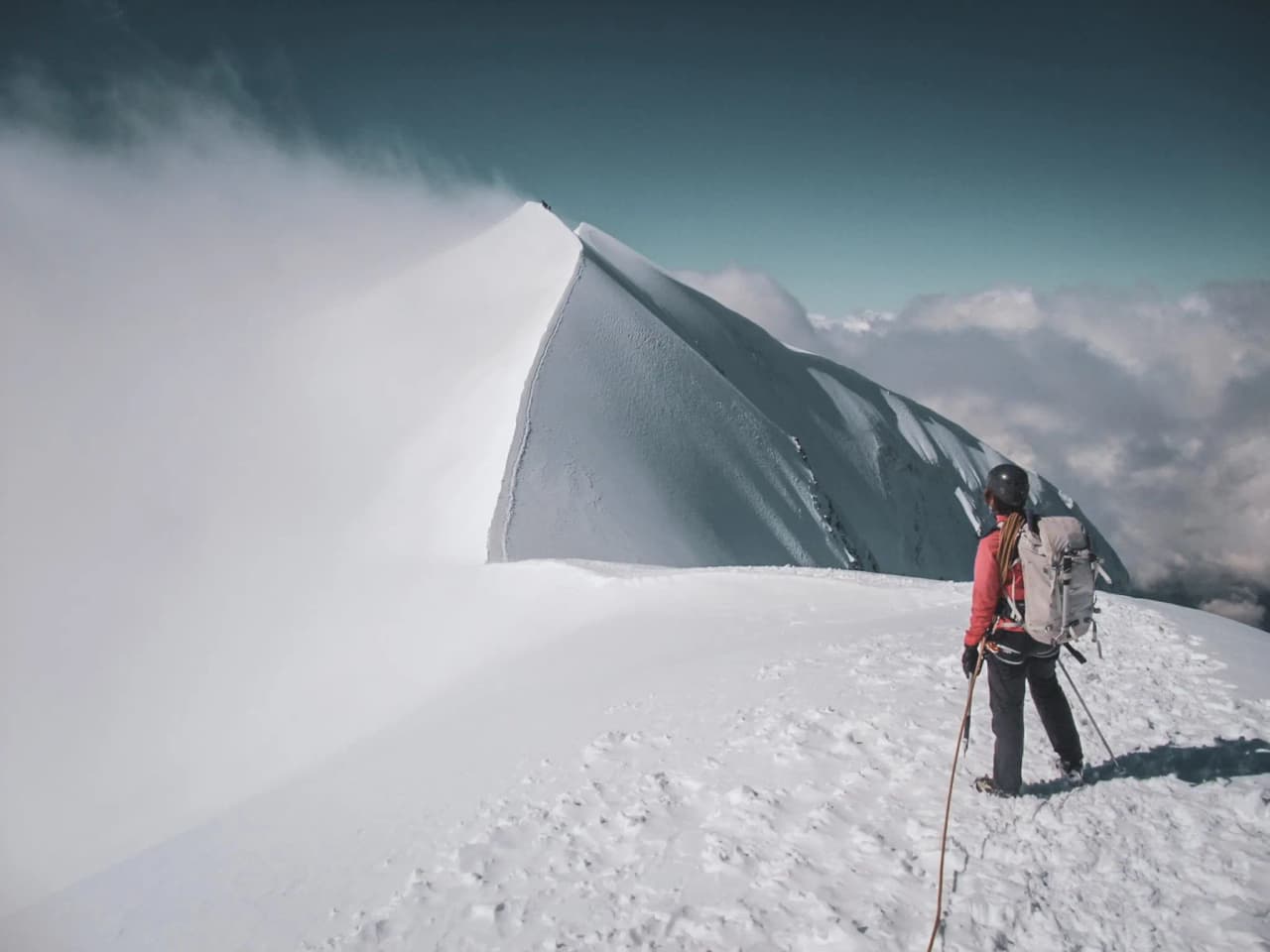 Een bergbeklimmer bekijkt de Dômes de Miage, omgeven door sneeuw en wolken, op de Mont Blanc.