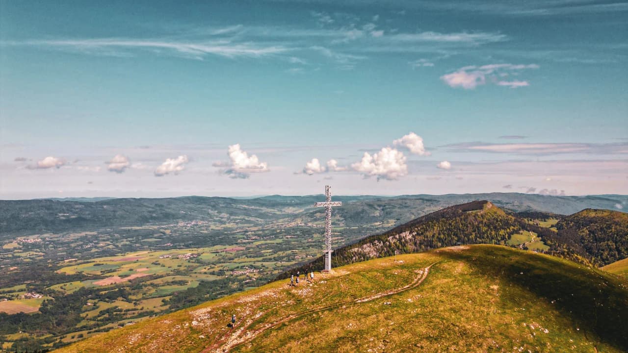 Panoramic view of the Jura massif, with a white cross on a green summit.