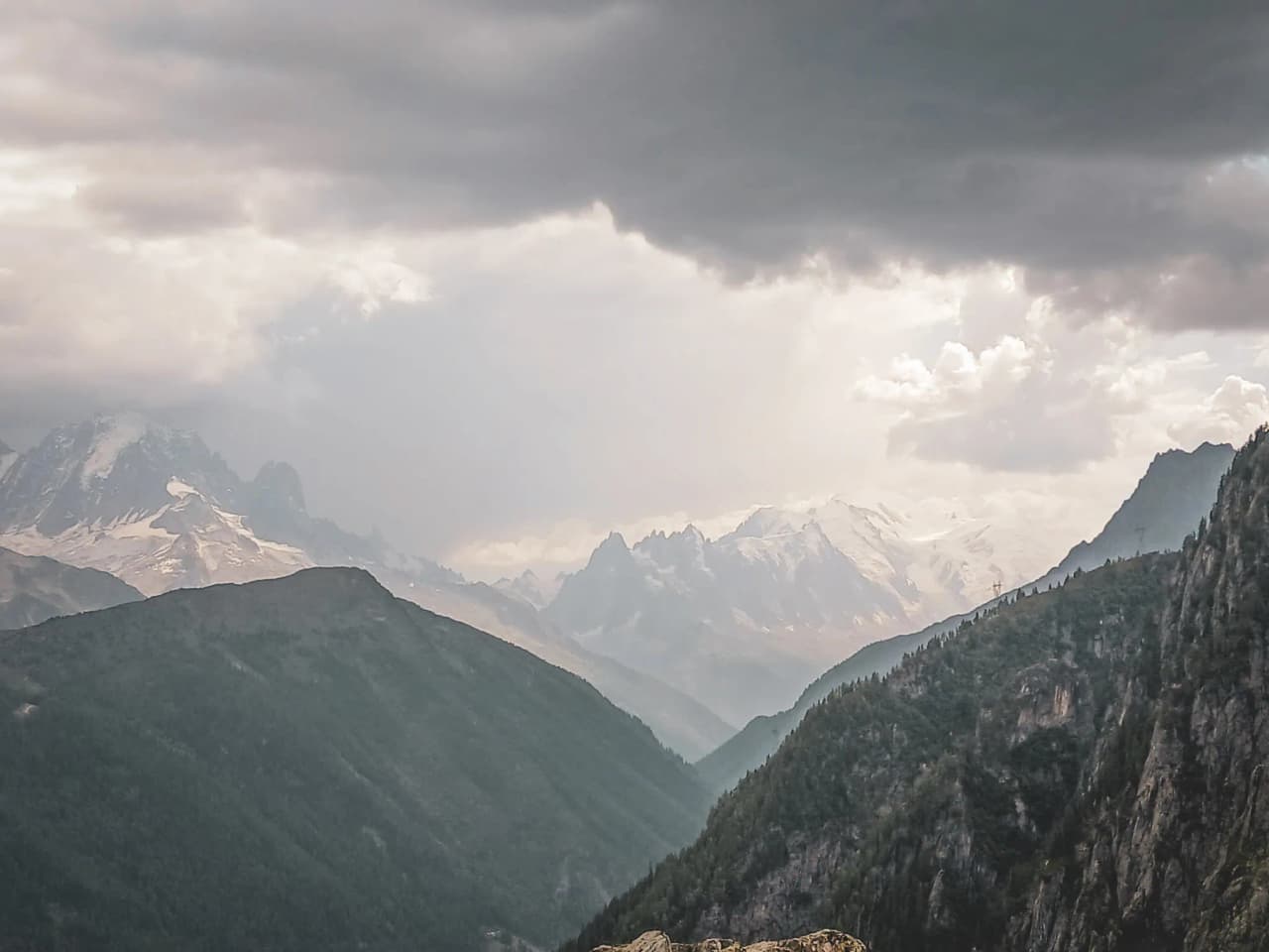 Paysage alpin majestueux avec montagnes, forêts verdoyantes et ciel nuageux, invitation à l'aventure.