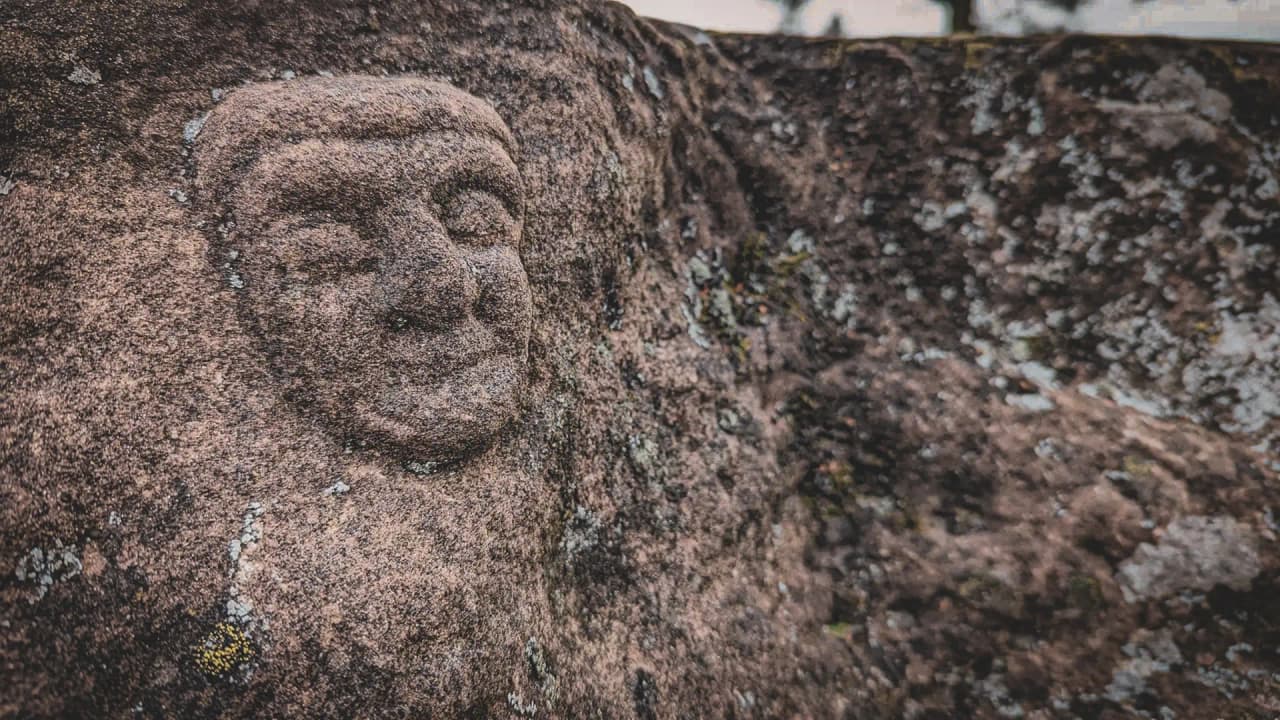 Visage sculpté dans la pierre, entouré de la nature sauvage des Vosges, invitant à l'exploration.