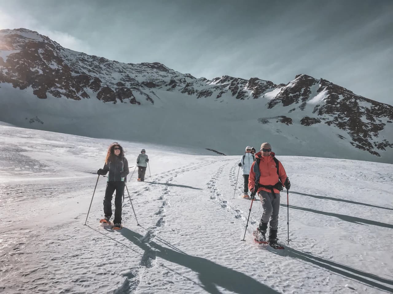 Groupe en randonnée raquette sur un glacier, paysages enneigés majestueux en arrière-plan.