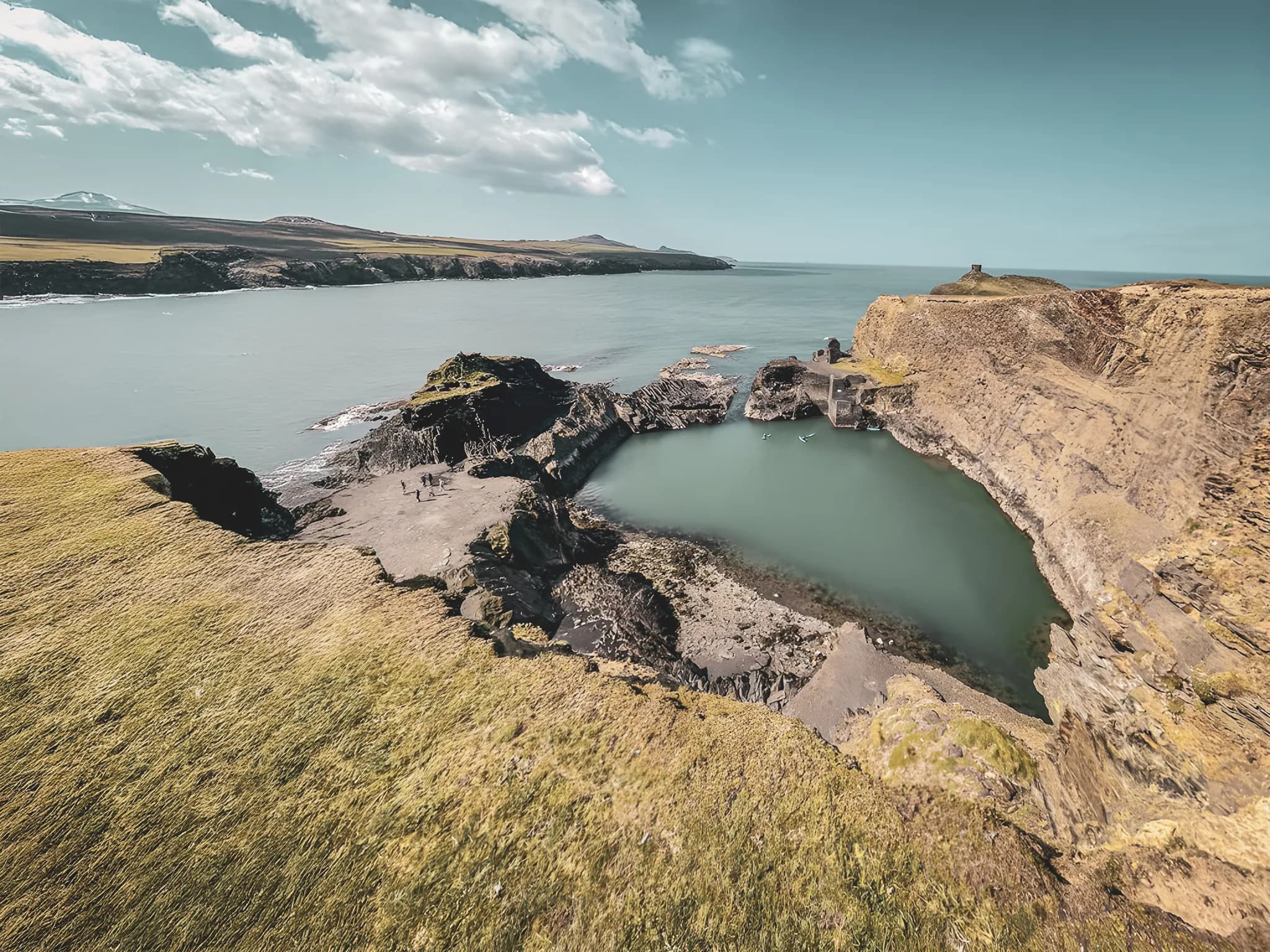 Côte sauvage galloise avec un lagon paisible et des falaises escarpées sous un ciel lumineux.