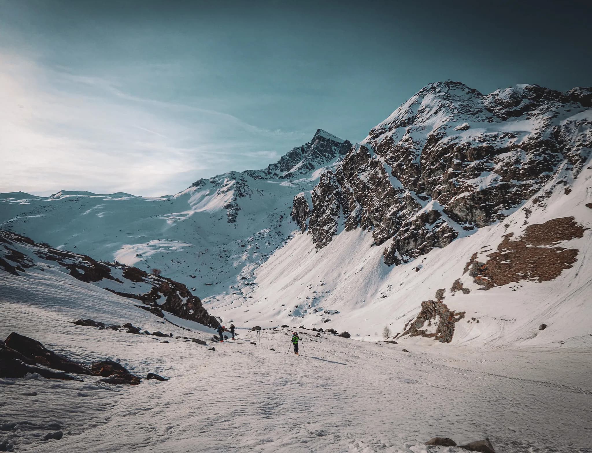 Un paysage alpin époustouflant, skieurs serpentinant dans un vallon enneigé sous des sommets majestueux.