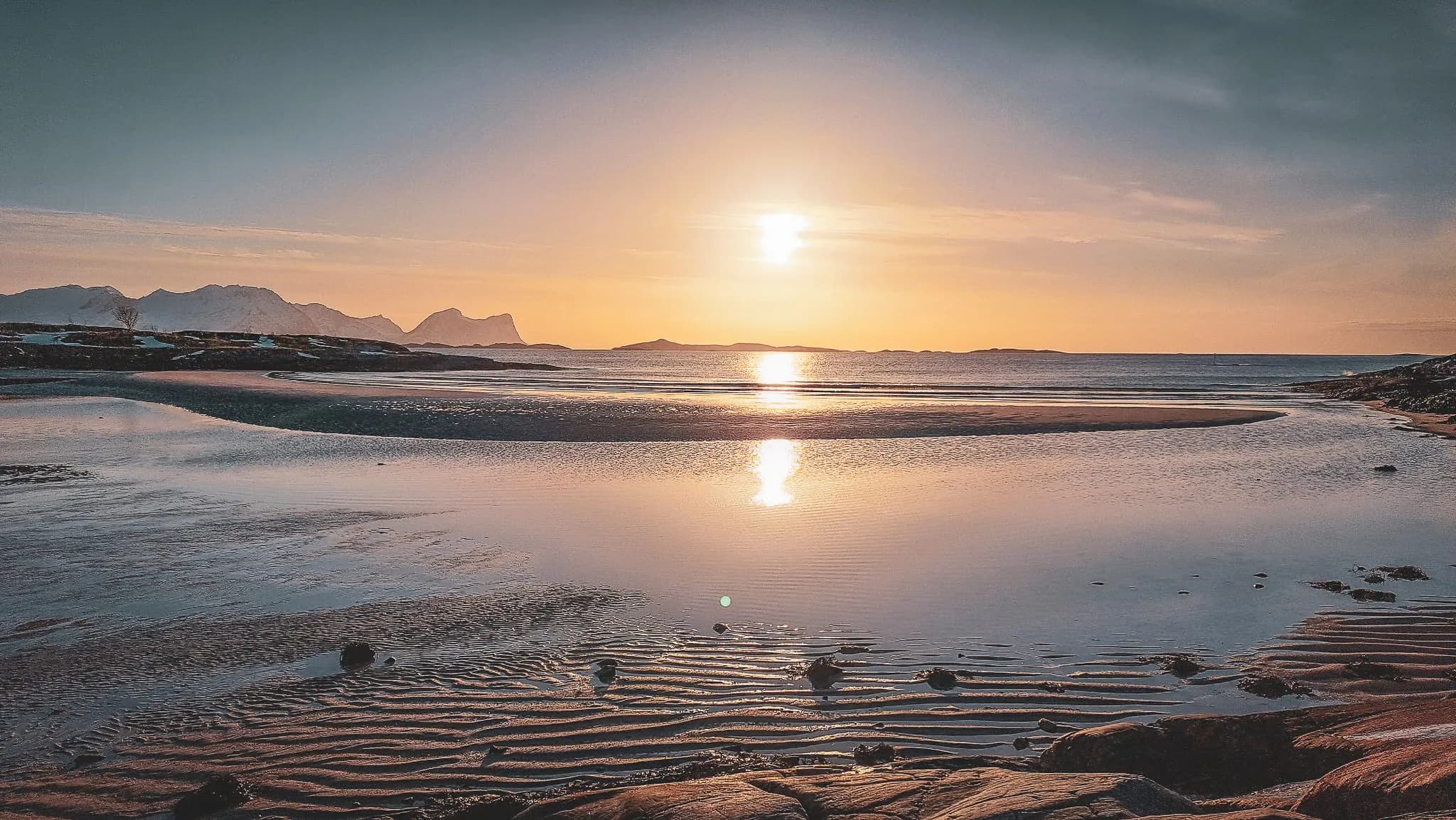 Sunset over the sea, golden reflections and mountains in the background, a peaceful atmosphere at Senja.