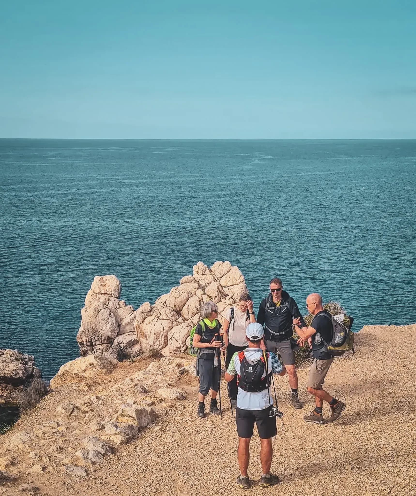 A group of hikers overlook the turquoise blue sea on Majorca, surrounded by breathtaking scenery.
