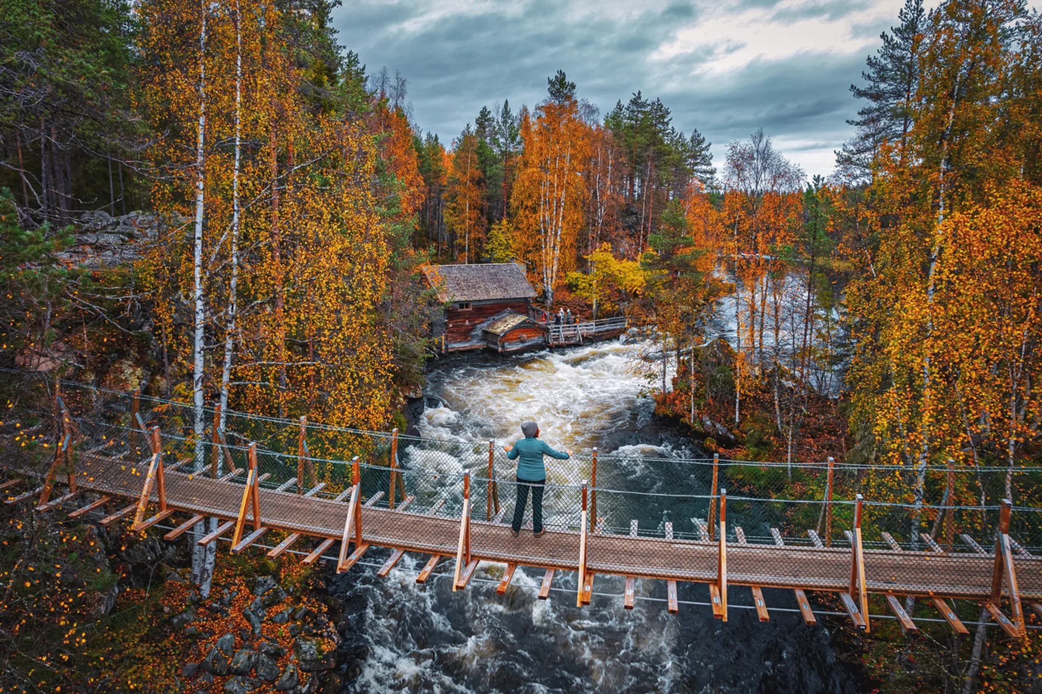 A suspension bridge over a tumultuous river, surrounded by colourful autumn forests.