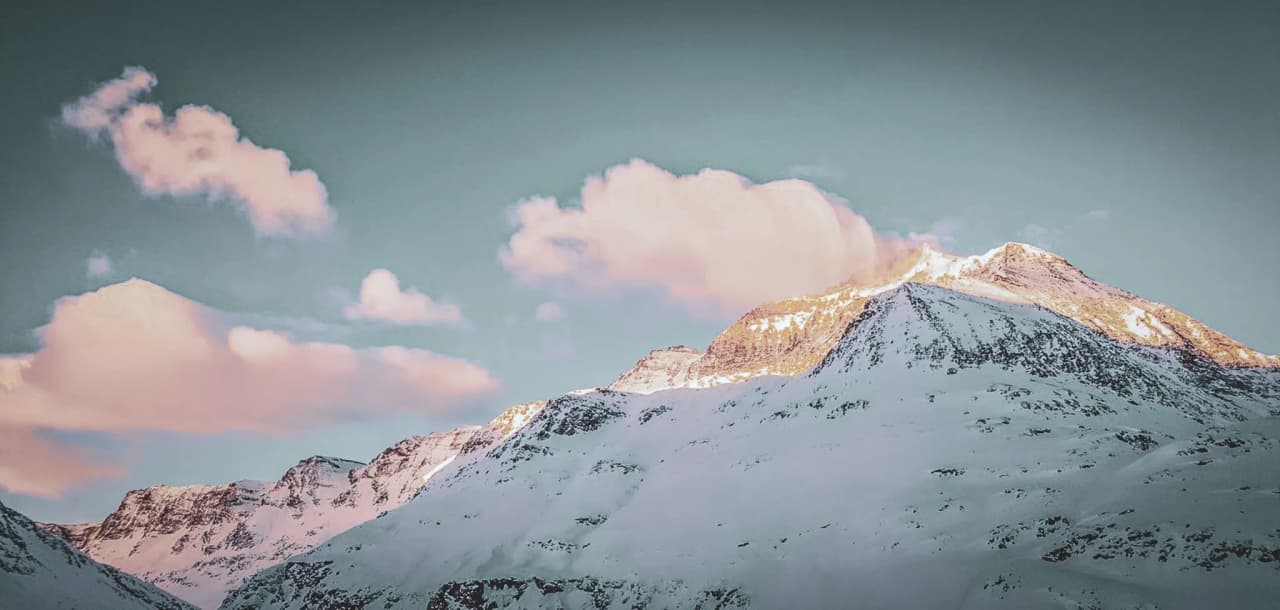 A majestic Alpine peak lit up by the sun, clear skies and pink clouds, an invitation to adventure.