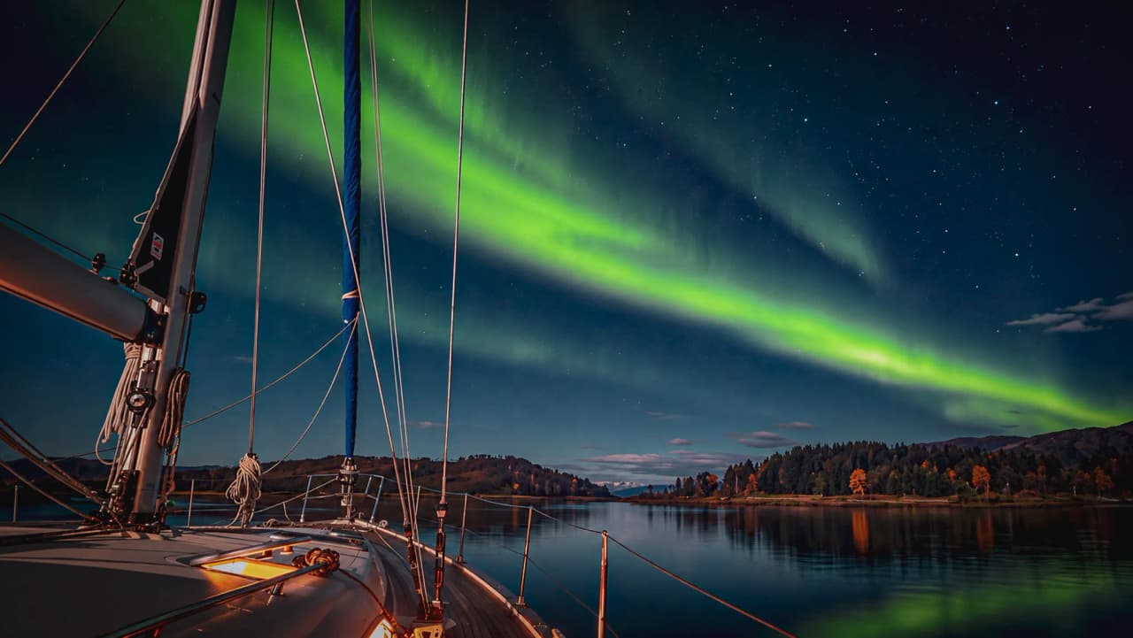 A sailing boat at anchor beneath the Northern Lights, the fjords of Tromsø, a starry sky and peaceful countryside.