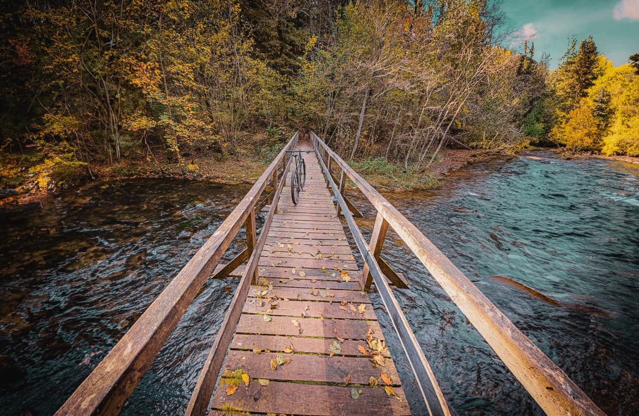 Pont en bois surplombant une rivière, entouré de forêts colorées pour une escapade nature.