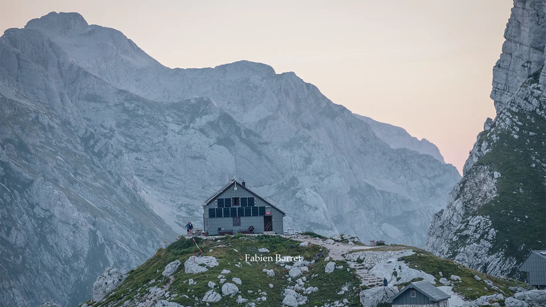 A mountainous landscape with layers of hills and peaks one on top of the other. The mountains are bathed in soft, misty light, creating an effect of depth. Shades of blue and