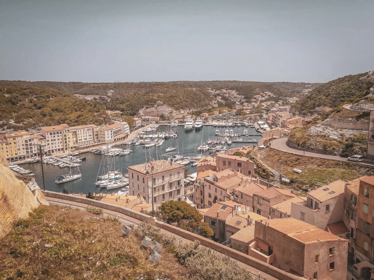 Vue panoramique de Bonifacio, port animé entouré de maisons colorées et de paysages naturels.