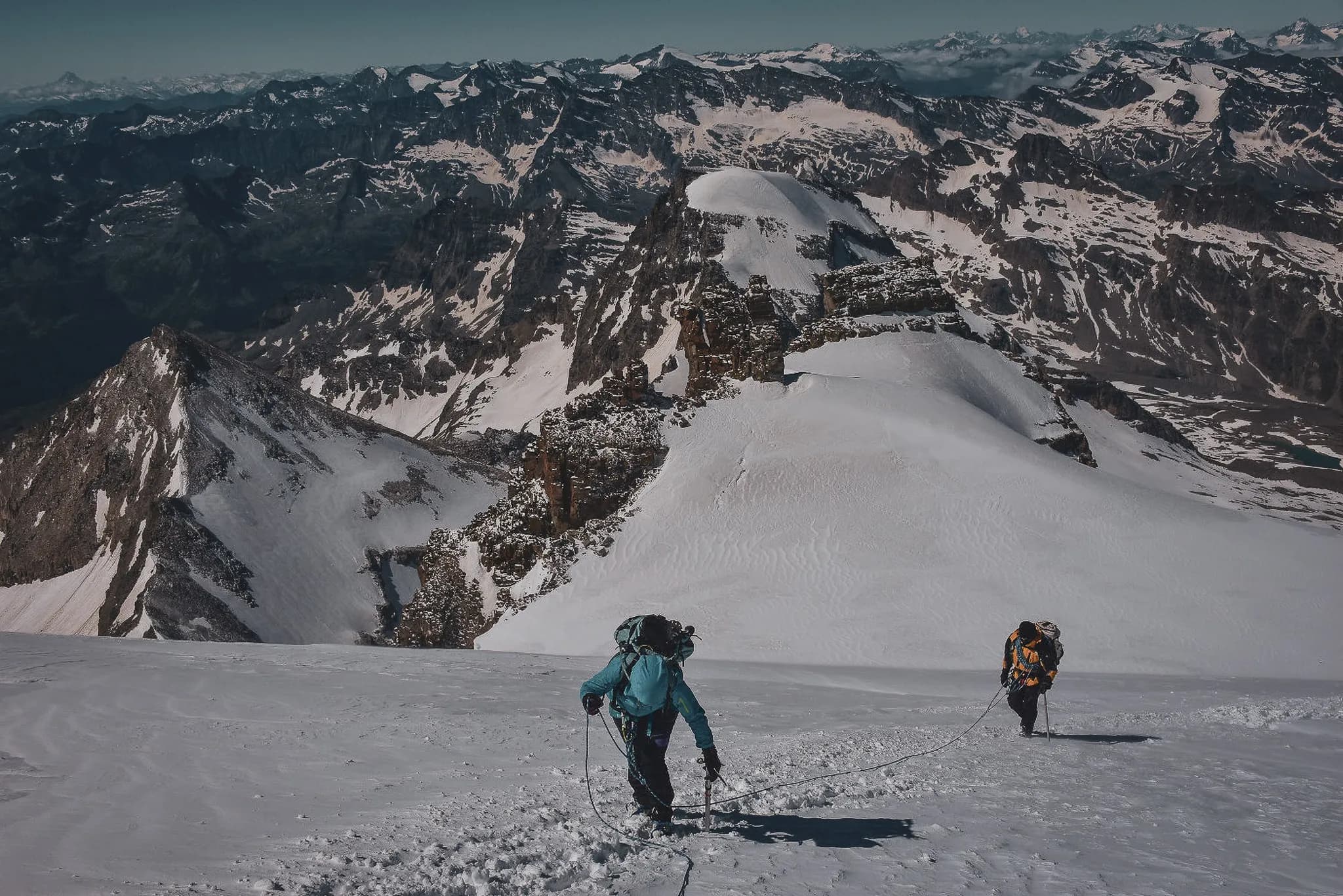 Twee alpinisten beklimmen Gran Paradiso door een besneeuwd berglandschap met steile toppen en ruige rotsen. Voorzichtig zetten ze hun tocht voort met hun klimuitrusting.