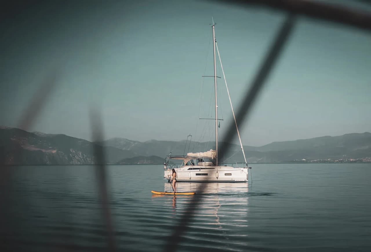 Un voilier tranquille sur des eaux calmes, avec un kayakiste et des montagnes en arrière-plan.