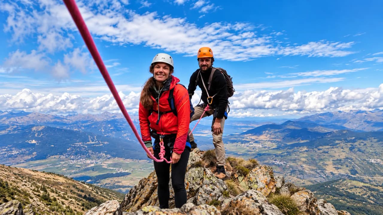 Een glimlachend stel tijdens het klimmen in de Pyreneeën, met een spectaculair panorama op de achtergrond.
