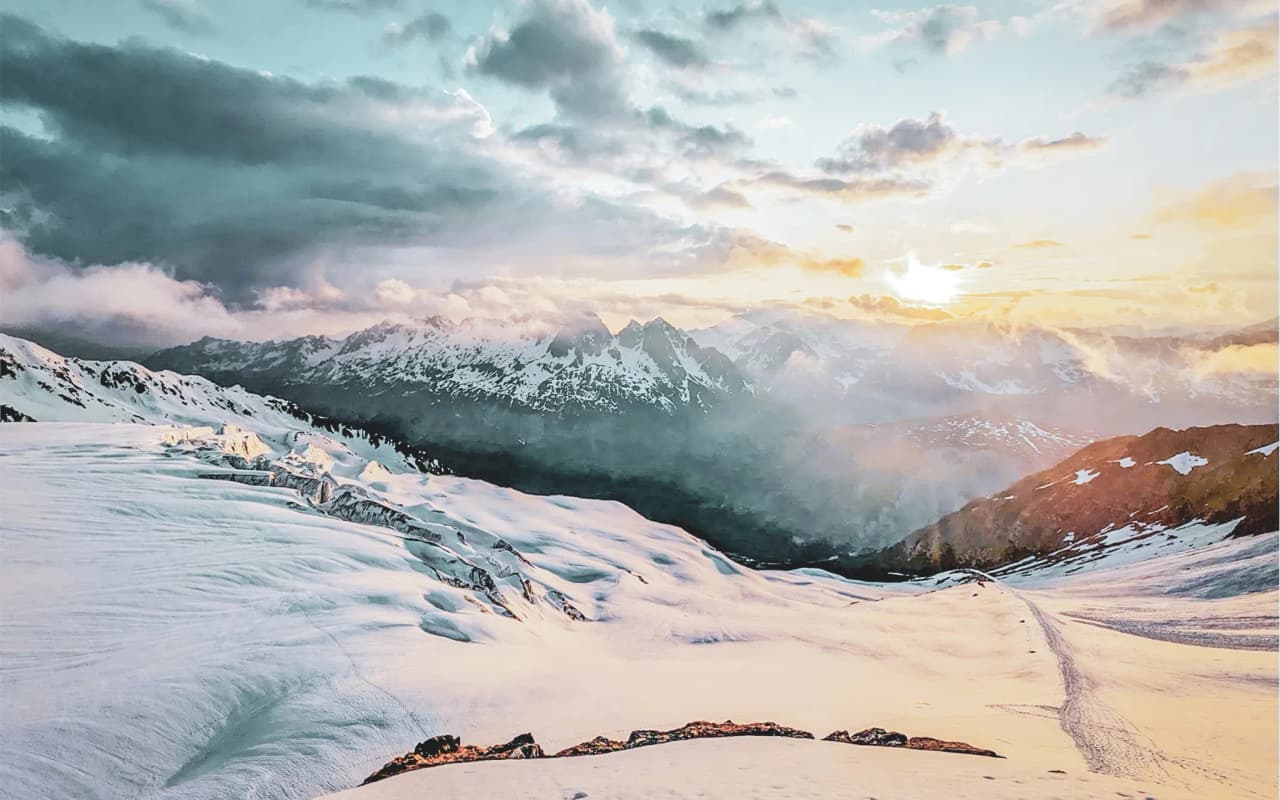 Un paysage enneigé à Chamonix, avec des montagnes majestueuses sous un ciel coloré au coucher de soleil.