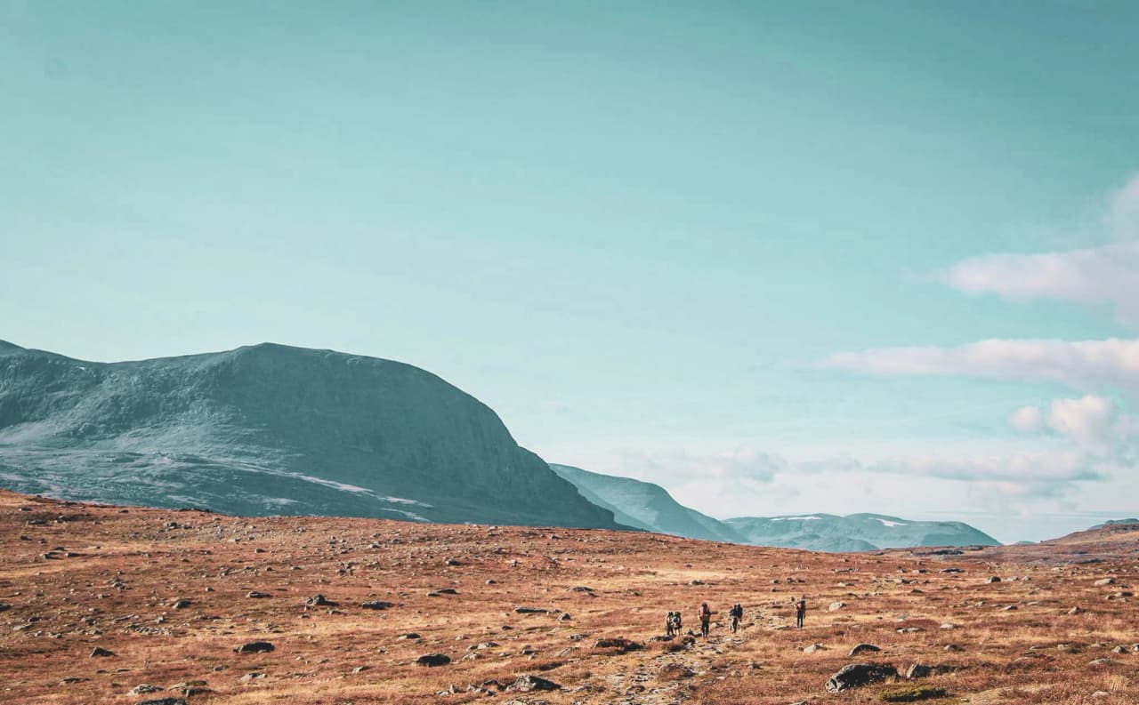 Hikers exploring the vast rolling landscapes of Swedish Lapland under a blue sky.