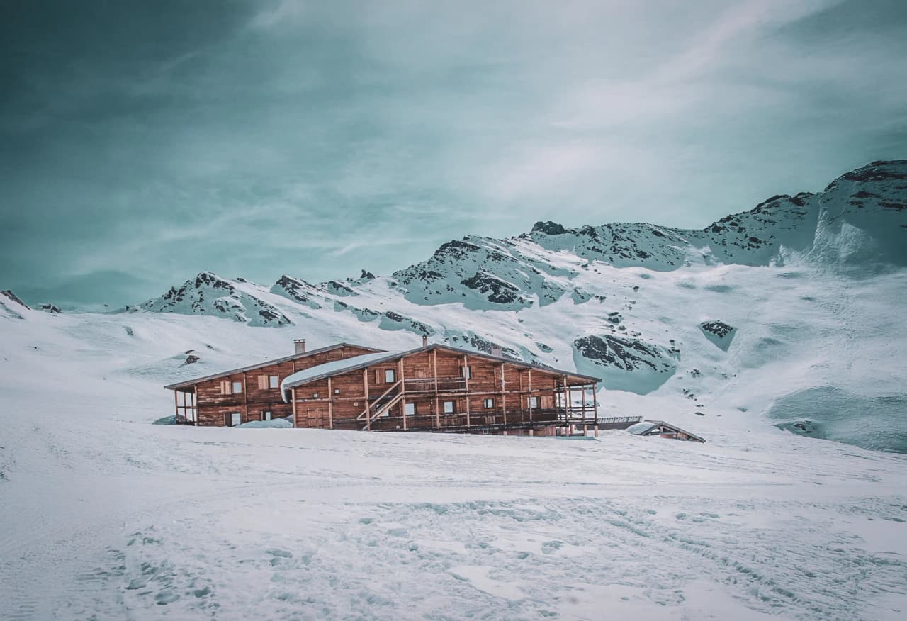 Cabane en bois entourée de montagnes enneigées, offrant une invitation au ski de randonnée.